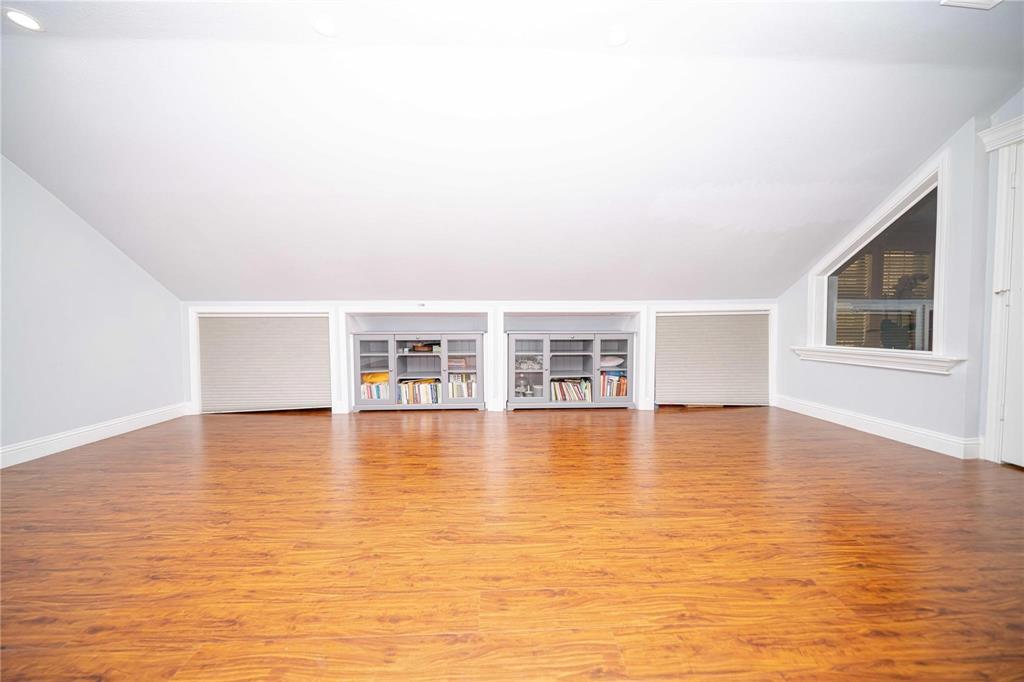 Sloped ceiling featuring recessed lighting, wood-finish flooring, built-in cabinetry with glass-front doors, and a triangular window