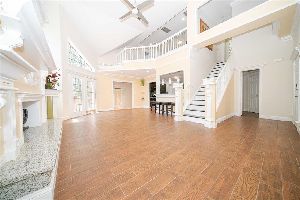 Two-story living area featuring vaulted ceilings, wood-finish flooring, a stone-surround fireplace, a mezzanine overlook with white railing, and a staircase with decorative millwork Two-story living area featuring vaulted ceilings, wood-finish flooring, a stone-surround fireplace, a mezzanine overlook with white railing, and a staircase with decorative millwork