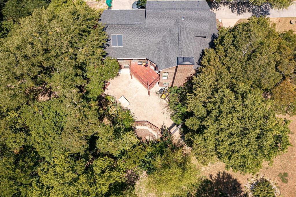Aerial perspective featuring a multi-level wood deck, expansive stone-paved patio, masonry chimney, and mature canopy trees