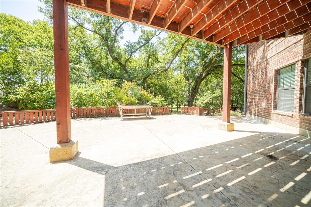 Covered patio featuring stamped concrete flooring, exposed wood ceiling joists, support pillars with stone bases, and perimeter wood fencing