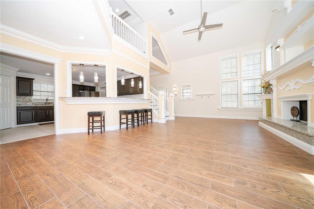 Open-concept living area featuring vaulted ceilings, wood-finish flooring, a stone-surround fireplace with a mantel, and multi-pane windows Open-concept living area featuring vaulted ceilings, wood-finish flooring, a stone-surround fireplace with a mantel, and multi-pane windows