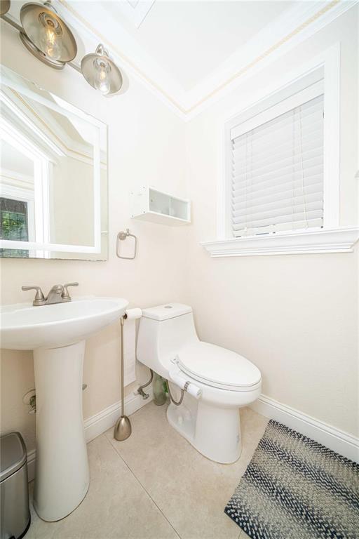 Pedestal sink with dual-handle polished chrome faucet, wall-mounted light fixture, single-piece elongated toilet, built-in shelving, and tile flooring