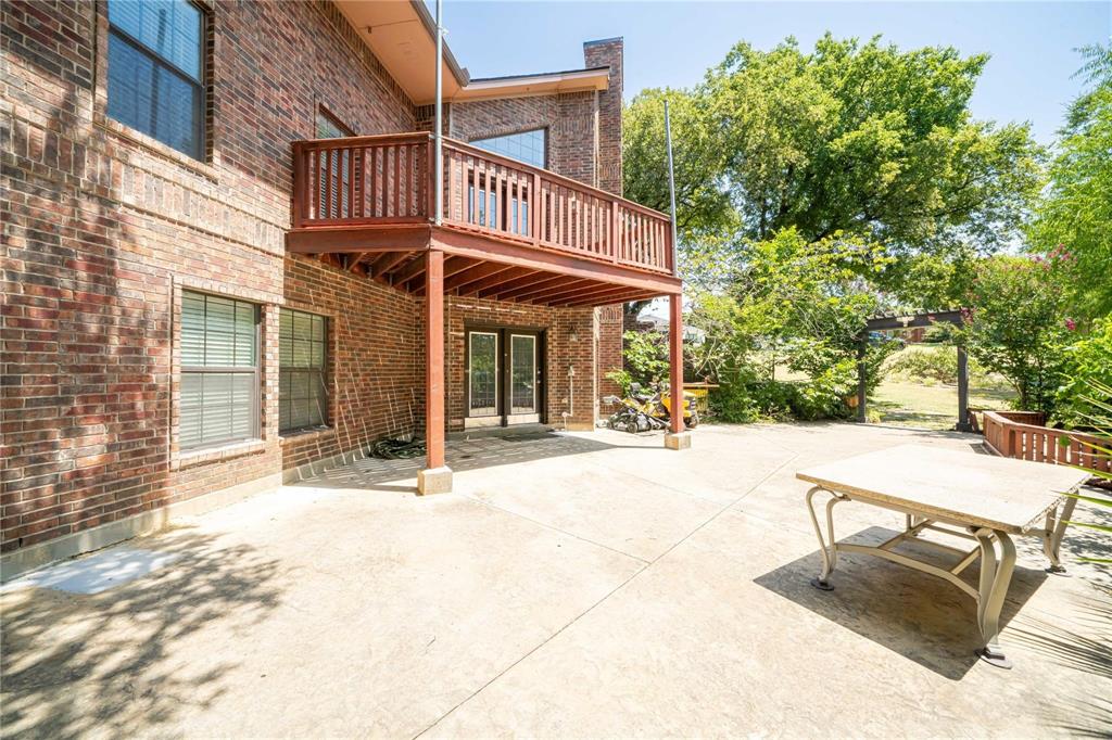 Multi-level red brick exterior featuring a covered concrete patio, an elevated wooden deck with railing, and a pergola