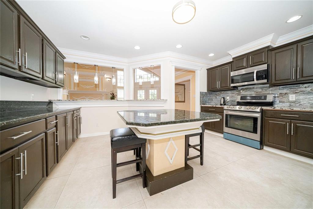Kitchen featuring dark wood cabinetry, stone countertops, stainless steel appliances, a tiled backsplash, and a central island with custom millwork Kitchen featuring dark wood cabinetry, stone countertops, stainless steel appliances, a tiled backsplash, and a central island with custom millwork