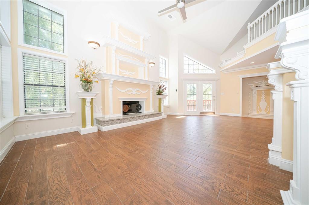 Vaulted ceilings with an upper-level mezzanine, wood-finish tile flooring, dual-story windows, and an ornate fireplace with a stone hearth Vaulted ceilings with an upper-level mezzanine, wood-finish tile flooring, dual-story windows, and an ornate fireplace with a stone hearth