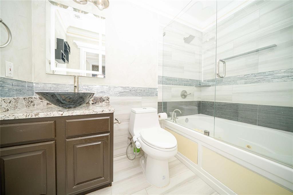 Dark wood-finish vanity with a stone countertop and a dark vessel sink, featuring a frameless glass-enclosed shower and tub combination with horizontal wall tiling