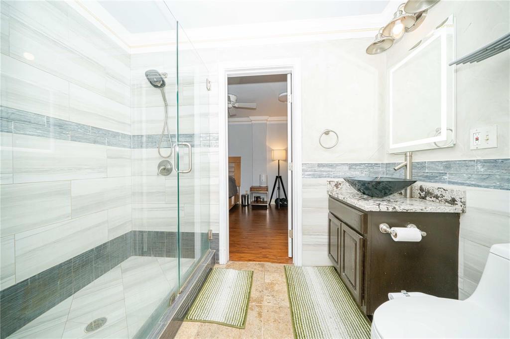 Walk-in shower with a glass enclosure and multi-setting showerhead, stone-finish countertop, dark wood-finish cabinetry, rectangular vessel sink, and illuminated mirror
