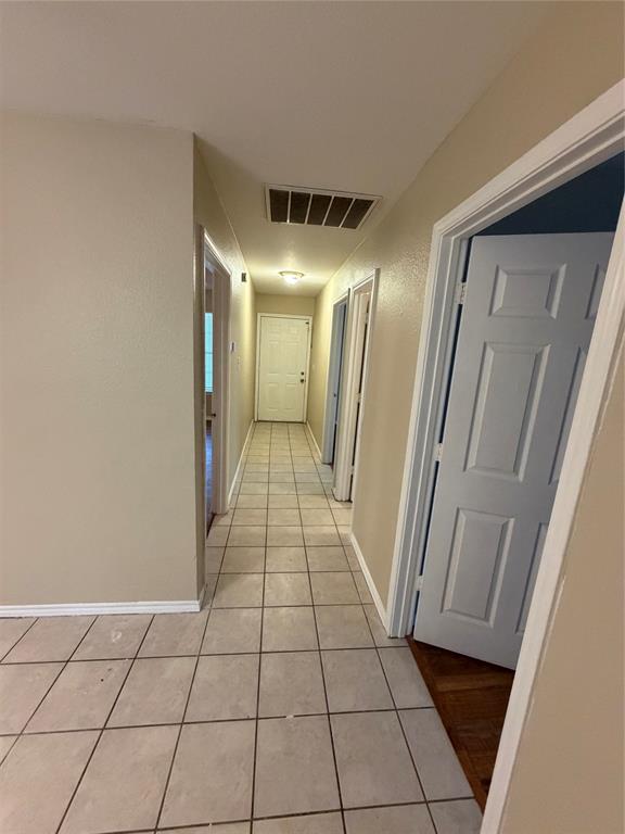 Hallway featuring neutral-toned tile flooring and multiple interior doors with multi-panel designs