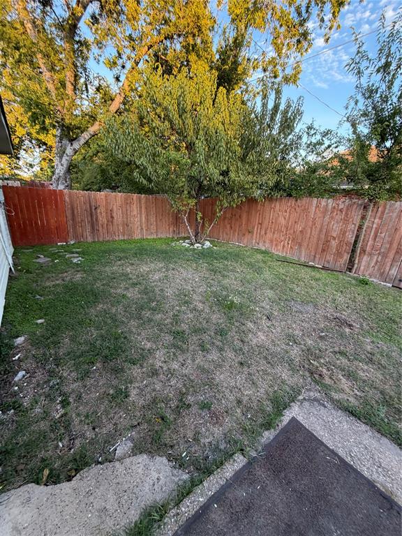 Backyard featuring a grass lawn, perimeter wood fencing, and mature trees