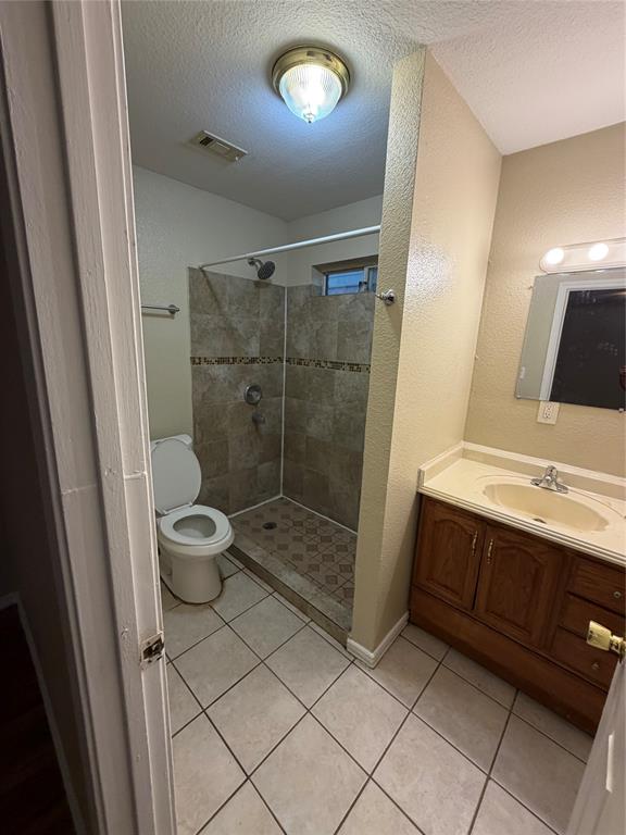 Bathroom featuring a walk-in shower with tile surround, wood-finish cabinetry, integrated sink countertop, and tiled flooring
