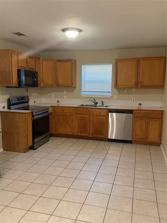 Kitchen featuring wood cabinetry, stainless steel appliances, tile flooring, a dual-basin sink, and a tiled backsplash Kitchen featuring wood cabinetry, stainless steel appliances, tile flooring, a dual-basin sink, and a tiled backsplash