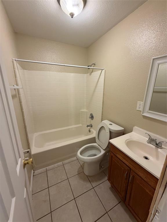 Bathroom featuring a tub-shower combination with tiled surround, a wooden vanity with an integrated sink, a wall-mounted mirror, and tile flooring