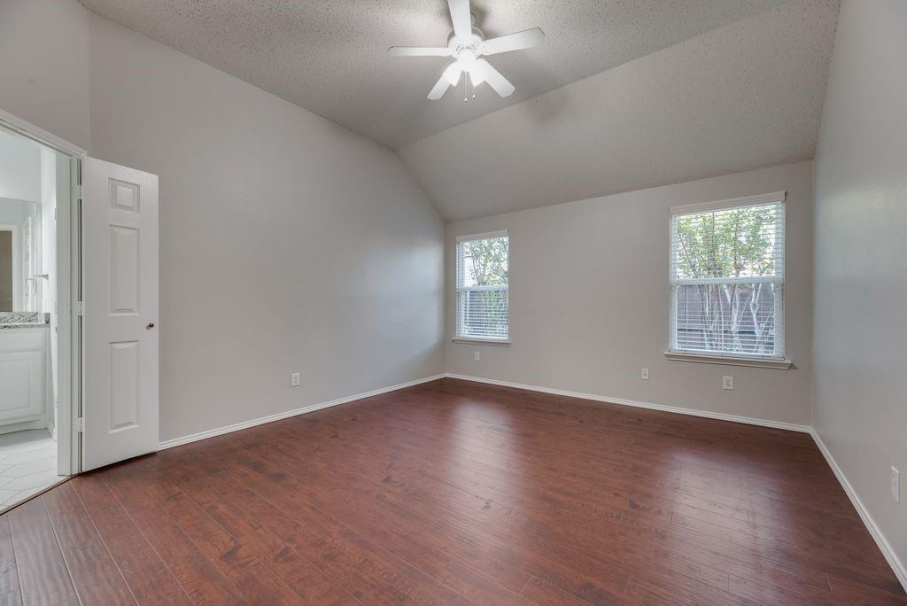 Spacious primary bedroom with wood floors, ceiling fan, raised ceiling, and ensuite bath.