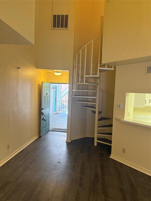High-ceiling interior featuring wood-finish flooring, a white metal spiral staircase, and a pass-through opening to the kitchen
