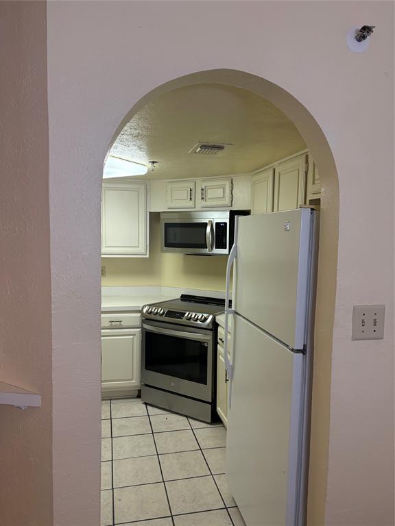 Arched doorway leading to a kitchen featuring light cabinetry, tile flooring, and stainless steel appliances, including an over-the-range microwave and a slide-in range