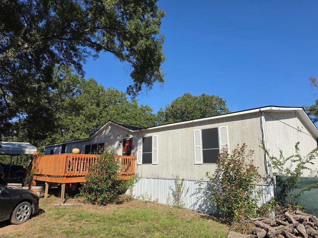 Exterior featuring a wood deck, vertical siding, shuttered windows, and a metal carport Exterior featuring a wood deck, vertical siding, shuttered windows, and a metal carport