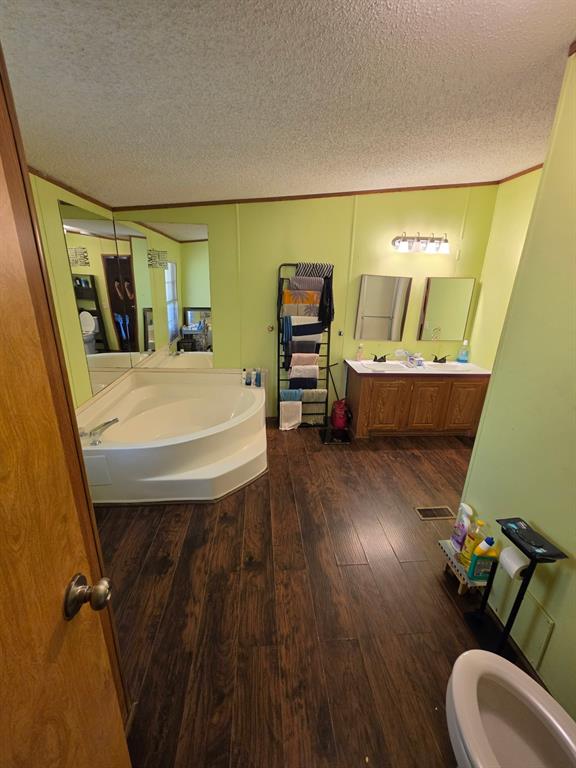 Bathroom featuring wood-finish flooring, a corner soaking tub, double-sink vanity with wood cabinetry, and wall-mounted vanity mirrors Bathroom featuring wood-finish flooring, a corner soaking tub, double-sink vanity with wood cabinetry, and wall-mounted vanity mirrors
