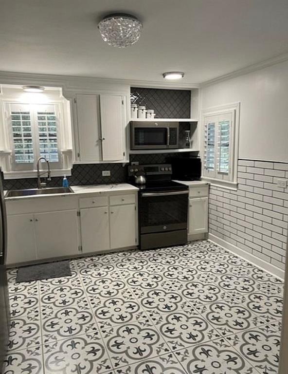Kitchen featuring white cabinetry, subway tile wall accents, patterned tile flooring, integrated stainless steel appliances, and plantation shutters