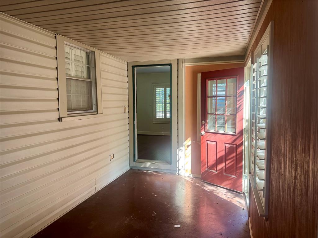 Covered porch featuring horizontal siding, wood-finish wall paneling, a red paneled entry door with glass light inserts, and windows with interior shutters