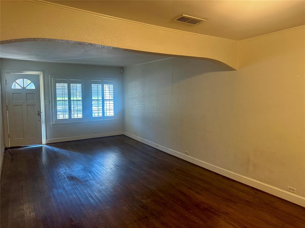 Interior featuring dark wood-finish flooring, a decorative arched wall detail, and a multi-pane entry door with an arched glass inset, complemented by plantation-style window shutters