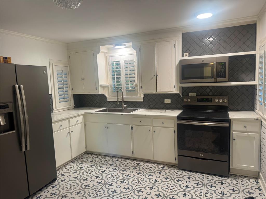 Kitchen featuring white shaker-style cabinetry, patterned tile flooring, dark-toned backsplash, stainless steel appliances, and a single-basin undermount sink