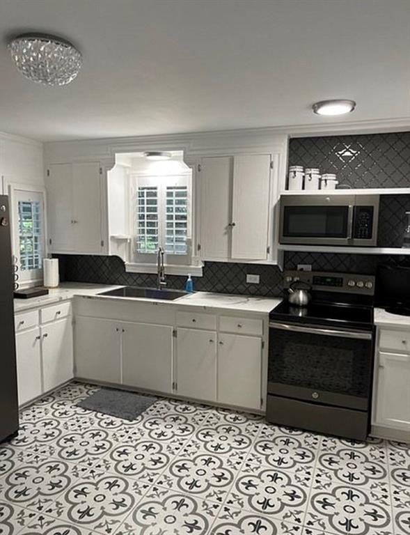 Kitchen featuring white cabinetry, patterned tile flooring, dark backsplash, stainless steel appliances, and interior window shutters