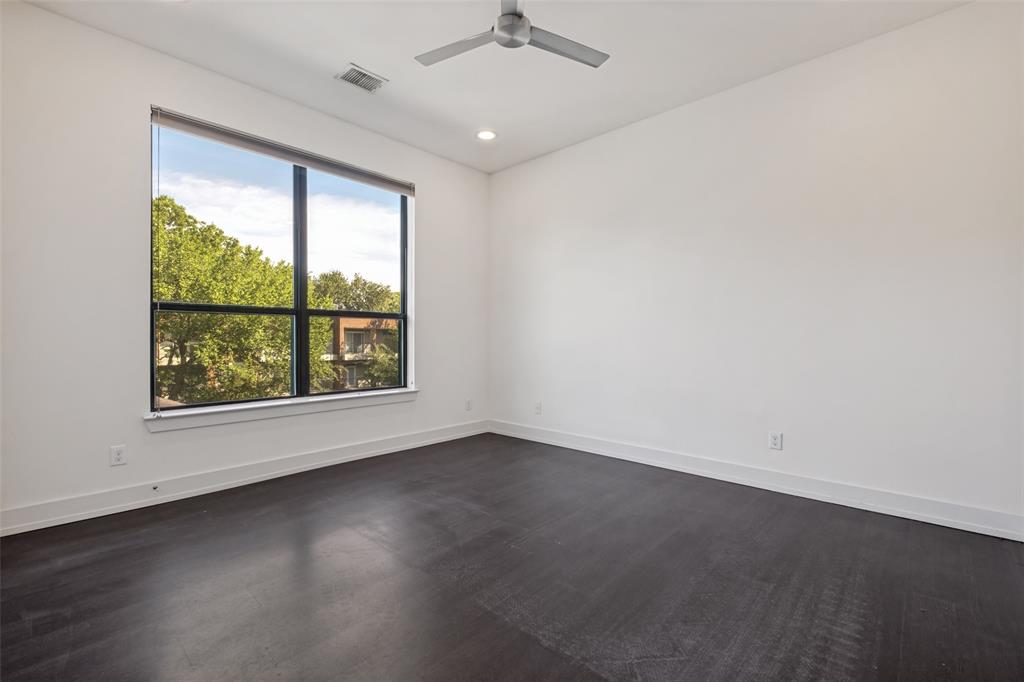 Dark wood-finish flooring, crisp white walls, large black-framed window, and a modern ceiling fan