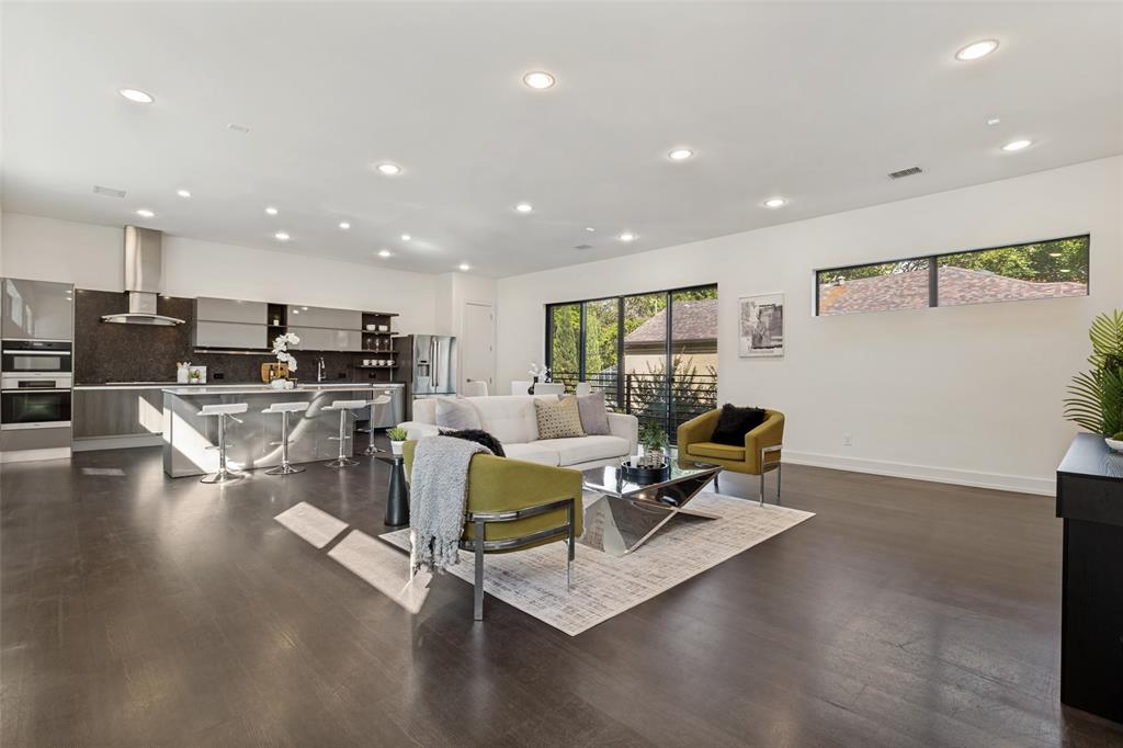 Open-concept living space featuring wood-finish flooring, recessed lighting, expansive sliding glass doors, and a modern kitchen with a large island and stainless steel range hood