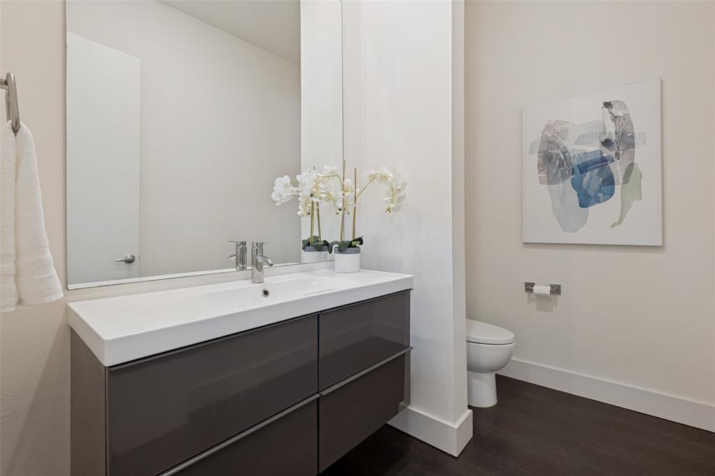Floating vanity featuring a high-gloss finish, white integrated rectangular sink, wall-spanning mirror, chrome-finish single-lever faucet, and wood-finish flooring
