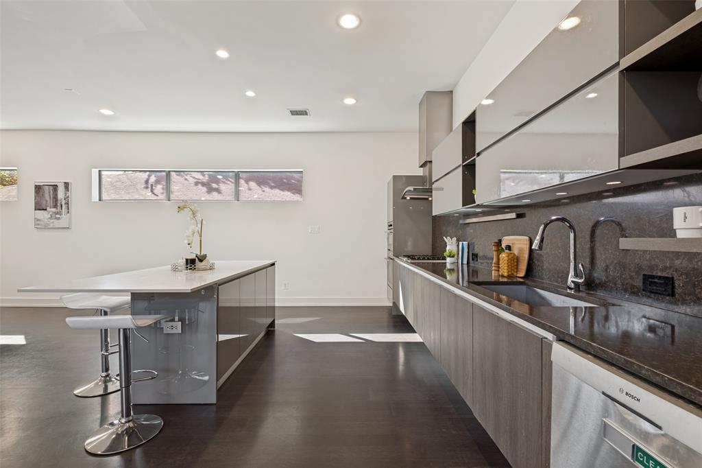 Modern kitchen featuring high-gloss cabinetry, a central island with a quartz countertop, stone-surfaced backsplash, integrated stainless steel appliances, and recessed ceiling lighting