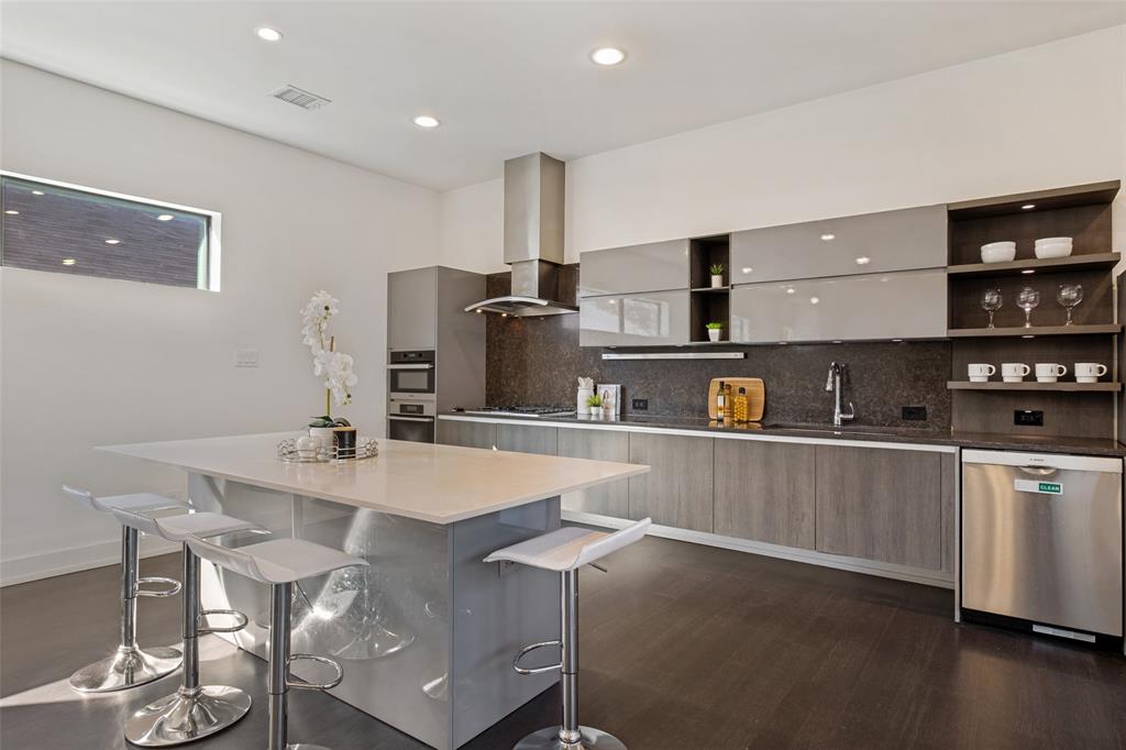 Modern kitchen featuring high-gloss gray cabinetry, a central island with a solid-surface countertop, stainless steel appliances, open shelving, and dark-toned wood-finish flooring
