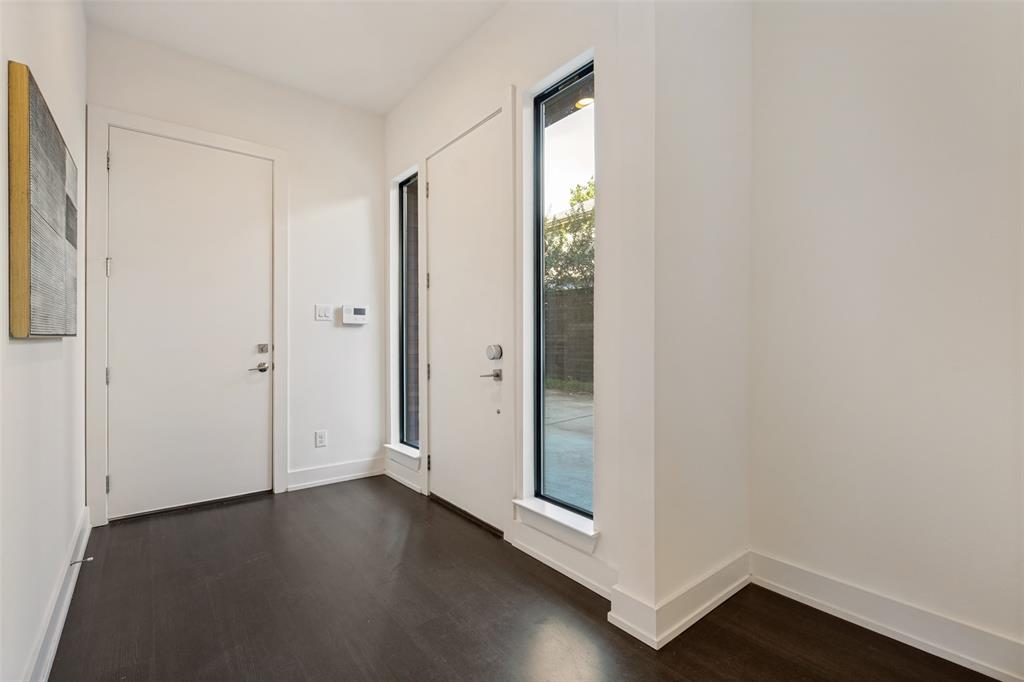 Entry area featuring dark wood-finish flooring, crisp white walls, vertical fixed-pane windows with black frames, and solid-core interior doors with satin nickel hardware
