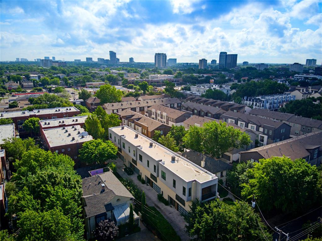 Aerial perspective of a multi-level residential complex featuring a flat roofline, neutral exterior cladding, balcony, and urban skyline backdrop