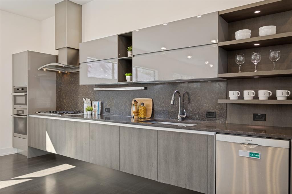 Modern kitchen featuring high-gloss cabinetry, stone-finish countertops, floating base cabinets, a stainless steel range hood, and open display shelving with integrated lighting