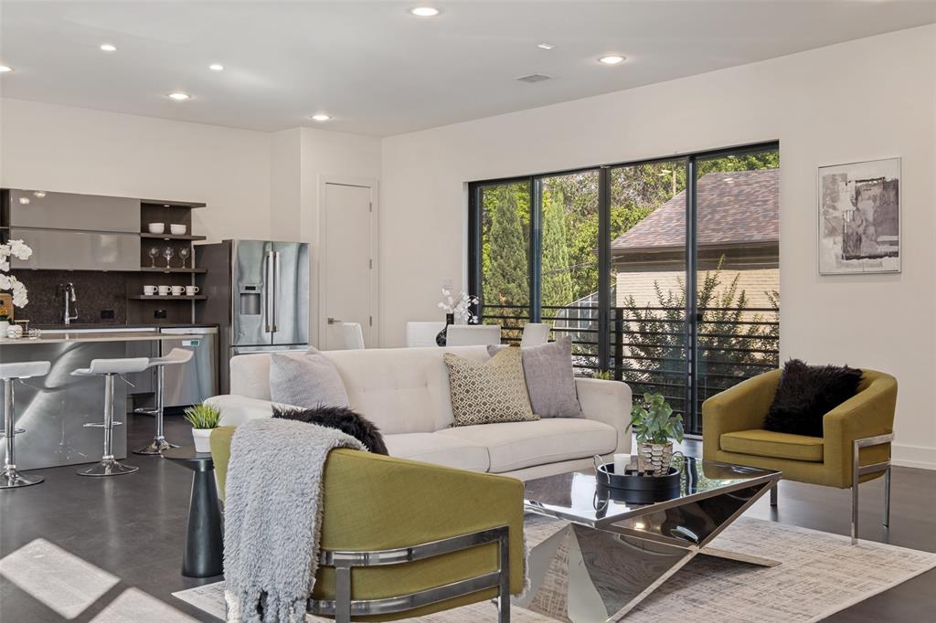 Open-concept kitchen featuring metallic-finish cabinetry, stone-surface countertops, and recessed lighting, complemented by expansive glass sliding doors with black framing