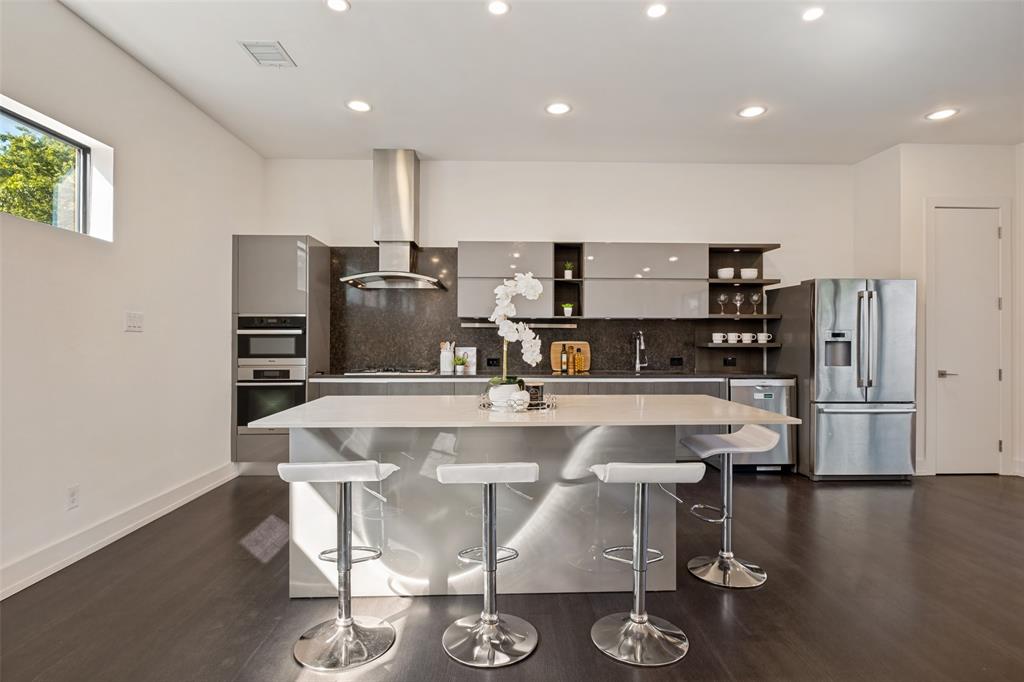 Contemporary kitchen featuring high-gloss cabinetry, a central island with a solid-surface countertop, stainless steel appliances, and dark wood-finish flooring