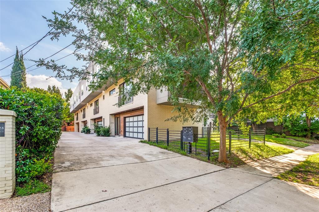 Modern multi-story exterior featuring light-toned brick masonry, grid-patterned garage doors, and metal perimeter fencing