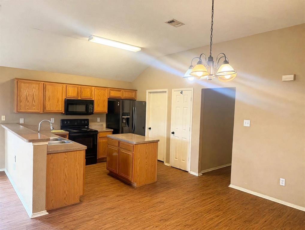 Kitchen featuring wood-finish cabinetry, a central island with a solid-surface countertop, wood-finish flooring, and vaulted ceilings Kitchen featuring wood-finish cabinetry, a central island with a solid-surface countertop, wood-finish flooring, and vaulted ceilings