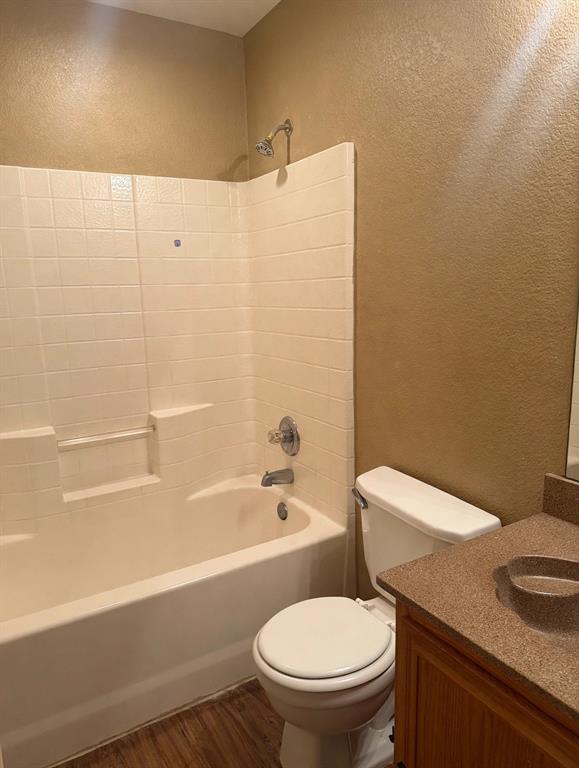 Bathroom featuring a tub-shower combination with tiled surround, wood-finish flooring, vanity with integrated basin, and chrome hardware