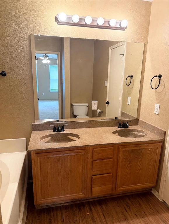 Dual-basin vanity featuring a stone-composite countertop, warm-toned wood cabinetry, matte black dual-handle faucets, and a full-width mirror with overhead light fixture Dual-basin vanity featuring a stone-composite countertop, warm-toned wood cabinetry, matte black dual-handle faucets, and a full-width mirror with overhead light fixture