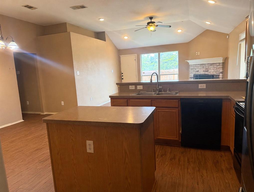 Kitchen featuring a central island, wood-finish cabinetry, vaulted ceilings with recessed lighting, and a brick-surround fireplace Kitchen featuring a central island, wood-finish cabinetry, vaulted ceilings with recessed lighting, and a brick-surround fireplace
