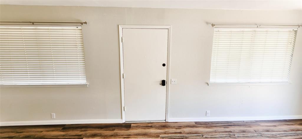 Interior wall featuring wood-finish flooring, two large windows with horizontal blinds, and a central entry door with an electronic deadbolt