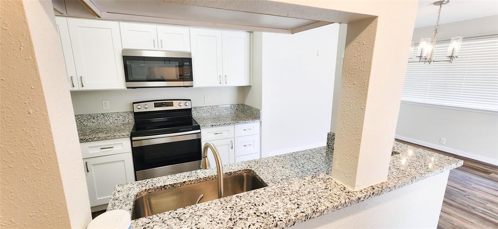 Kitchen featuring white cabinetry, stone countertops, stainless steel appliances, a stainless steel undermount sink with a gooseneck faucet, and wood-finish flooring