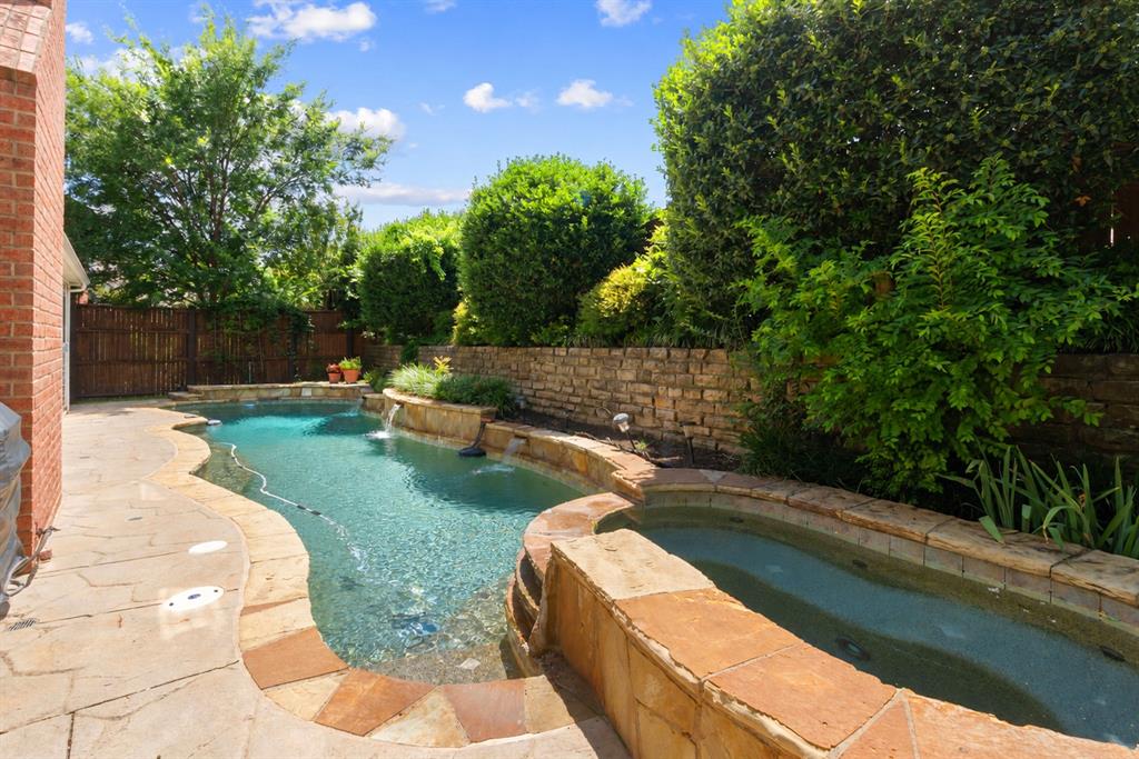 Freeform swimming pool featuring flagstone coping, an integrated spa, and stacked stone water features set within a fenced backyard Freeform swimming pool featuring flagstone coping, an integrated spa, and stacked stone water features set within a fenced backyard