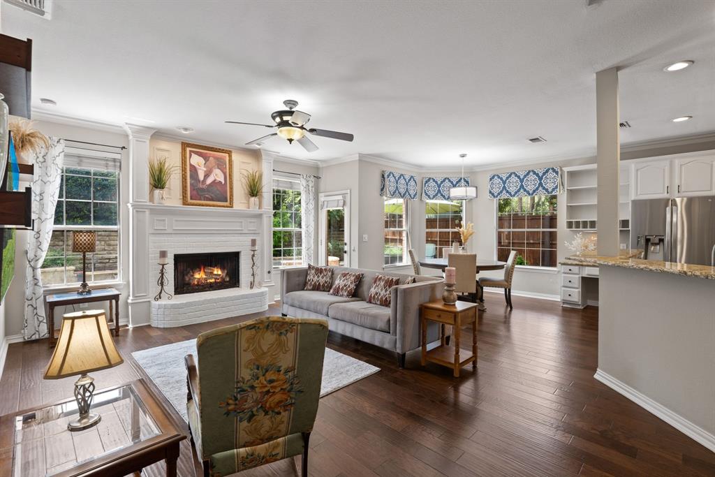 Open-concept interior featuring wood-finish flooring, a white brick fireplace with a decorative mantel, recessed lighting, and a kitchen peninsula with stone-finish countertops