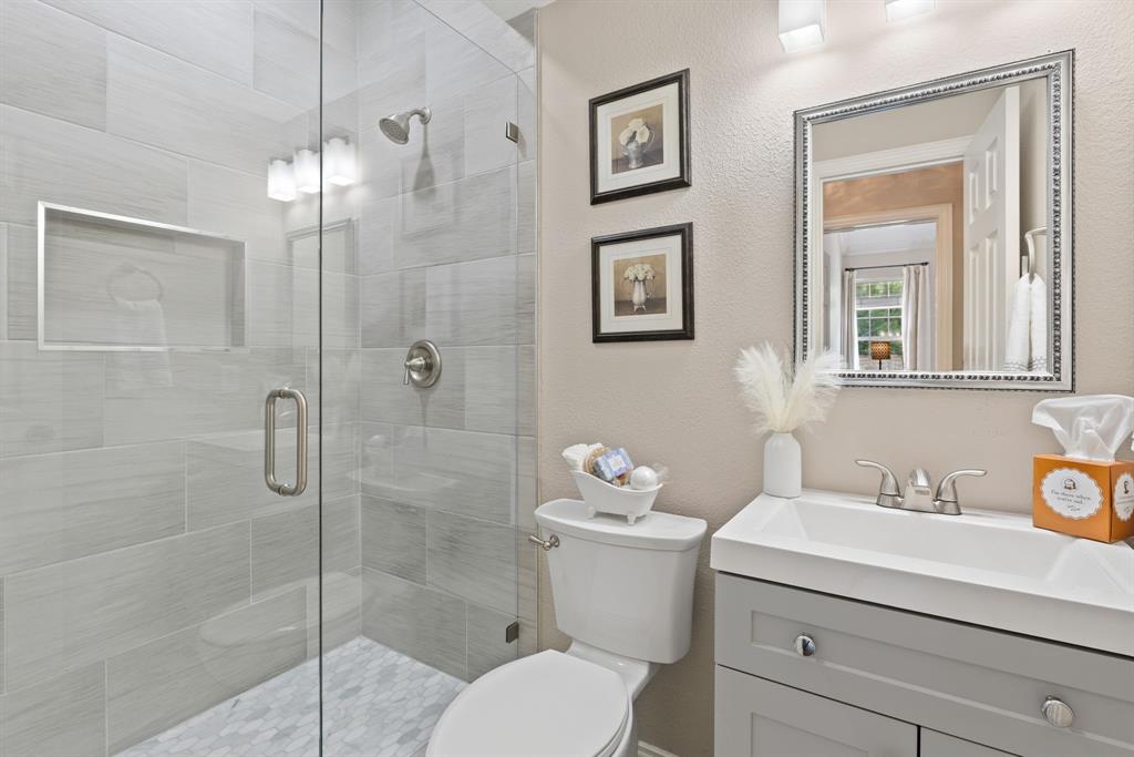 Walk-in shower with floor-to-ceiling ceramic tile, glass enclosure, and built-in recessed niche; vanity featuring a rectangular integrated sink and cabinet storage; wall-mounted vanity mirror