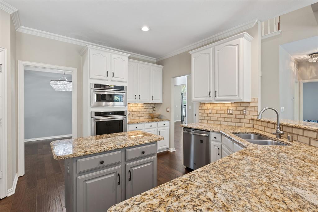 Kitchen featuring stone countertops, white upper cabinetry, a grey center island, stainless steel built-in double ovens, and a brick-pattern backsplash
