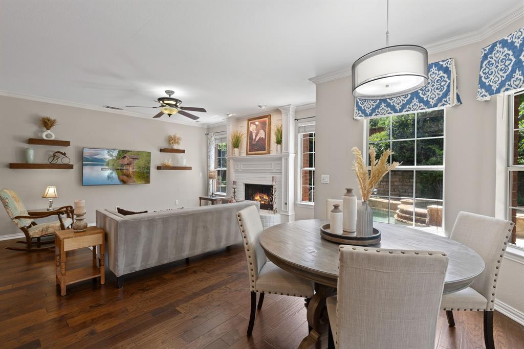Living area featuring wood-finish flooring, a wood-burning fireplace with an ornate mantel, floating wall shelves, a ceiling fan, and multi-pane windows