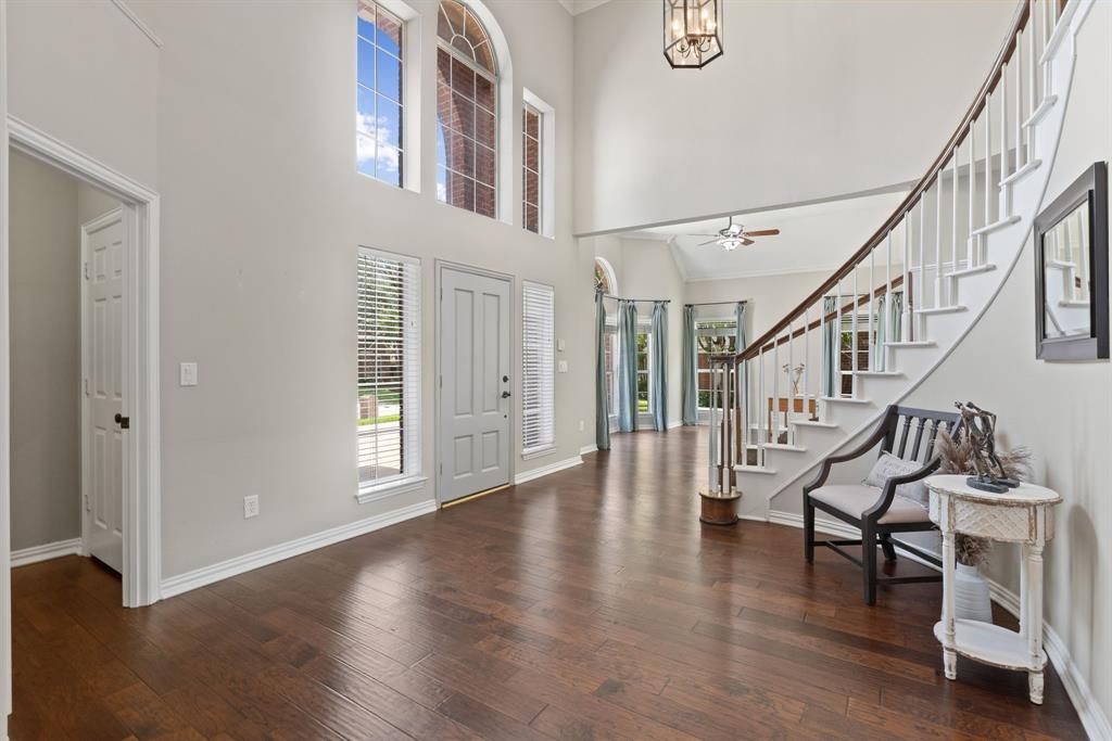 Foyer featuring vaulted ceilings, wood-finish flooring, a sweeping staircase with white balusters, multi-pane arched windows, and a suspended lantern-style fixture Foyer featuring vaulted ceilings, wood-finish flooring, a sweeping staircase with white balusters, multi-pane arched windows, and a suspended lantern-style fixture