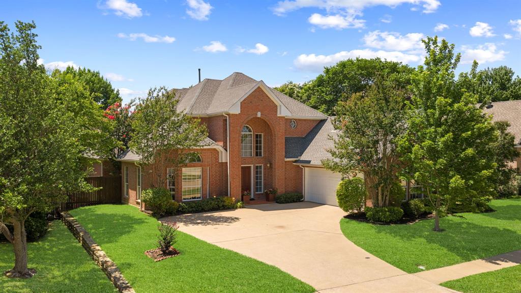 Brick exterior residence featuring an arched entryway, a steep-pitched roof, an attached two-car garage, and manicured landscaping with stone-retaining walls